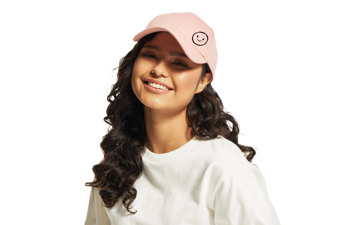 Header image of a young woman with curly hair wearing a custom pink hat from Hollywood Prints. The hat features a smiley face logo, showcasing the customizable headwear options available on our website.