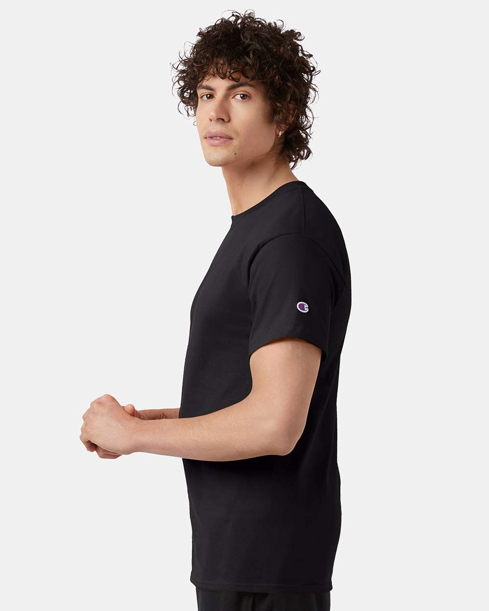 Curly headed male standing sideways wearing black Champion short sleeve t-shirt