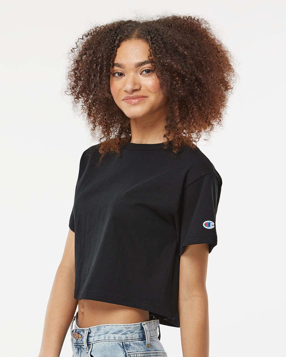 Woman with curly poofy hair standing sideways wearing a black Champion crop top.