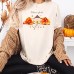 A woman wearing a shirt of Gillmore ghouls in front of a gazebo with fall leaves surrounding them.