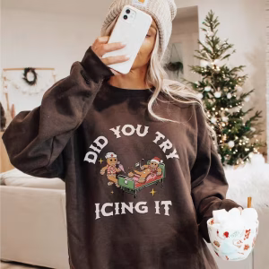 Woman wearing the Funny Christmas Sweatshirt "Did You Try Icing It?" with a beanie, taking a selfie in front of a Christmas tree.